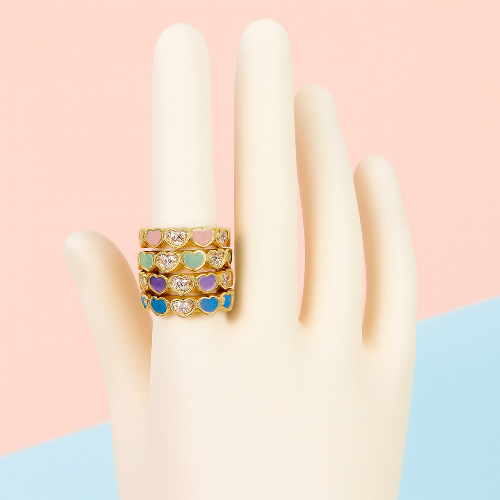 Multicolored heart-shaped ring on a hand against a pink background