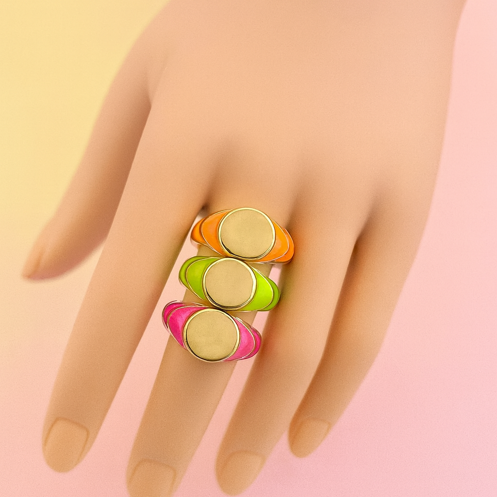 Hand wearing a colorful ring with pink, green, orange, and gold bands on a gradient background