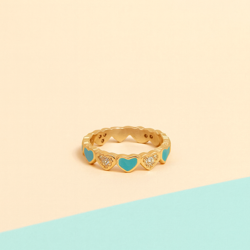 Gold ring with blue heart-shaped stones on a two-tone beige and blue background