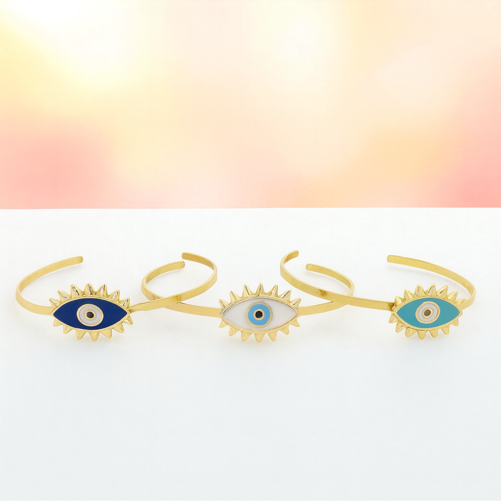 Three gold evil eye cuffs on a gradient background