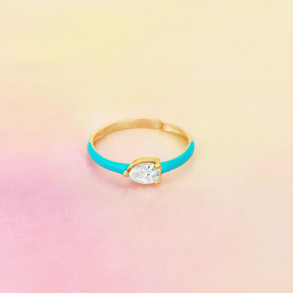 Gold ring with a pear-shaped gemstone on a pastel gradient background