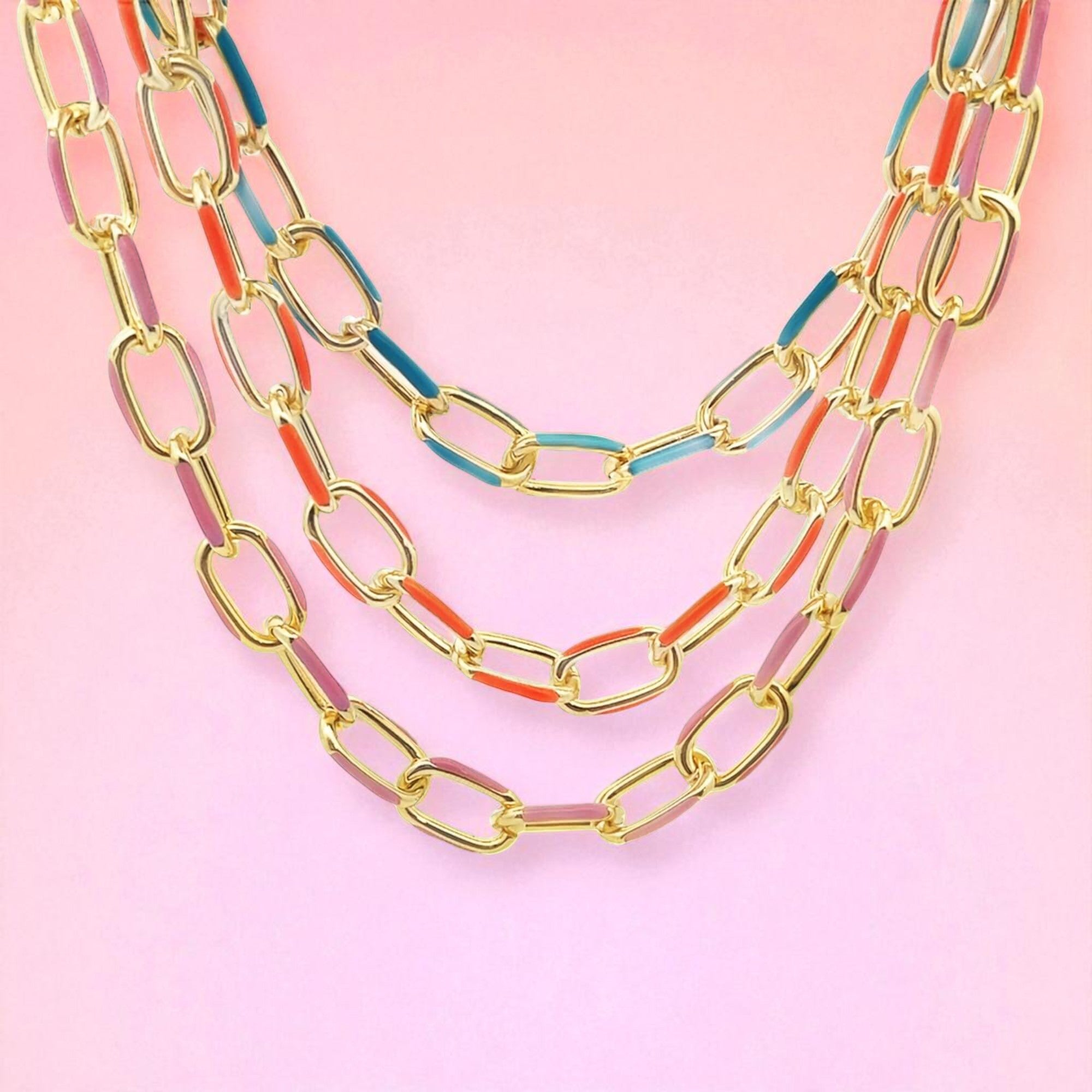 Gold chain necklaces with colorful accents on a pink background